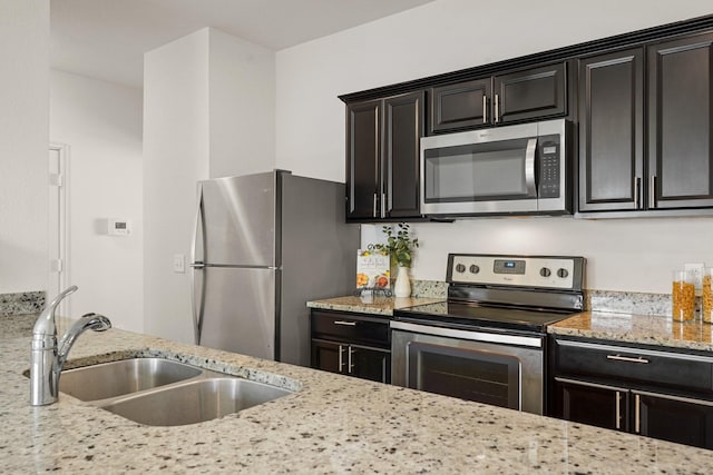 kitchen featuring dark cabinets, light stone countertops, stainless steel appliances, and a sink