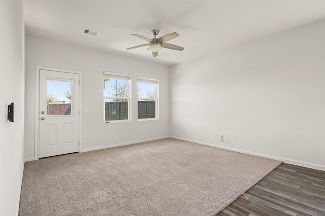 empty room featuring visible vents, dark wood finished floors, dark carpet, baseboards, and ceiling fan