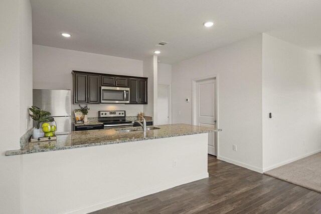 kitchen featuring visible vents, a sink, appliances with stainless steel finishes, light stone countertops, and dark wood-style flooring