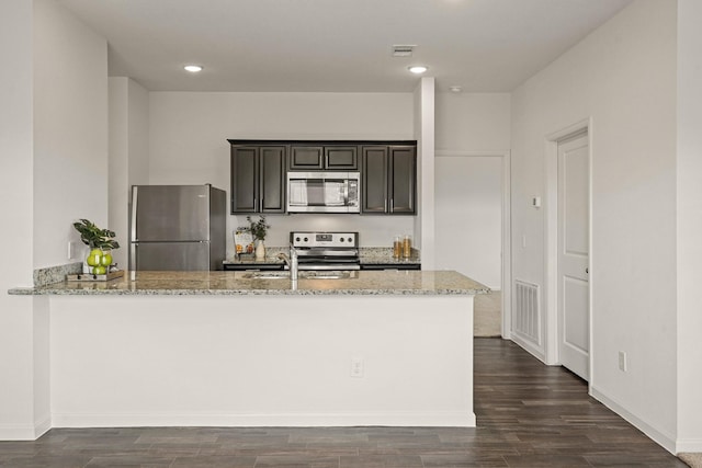 kitchen with light stone countertops, visible vents, dark wood finished floors, a peninsula, and appliances with stainless steel finishes