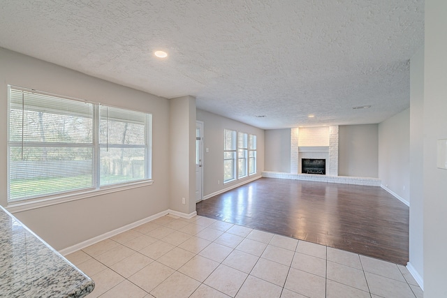 unfurnished living room with light tile patterned floors, a fireplace, baseboards, and a textured ceiling