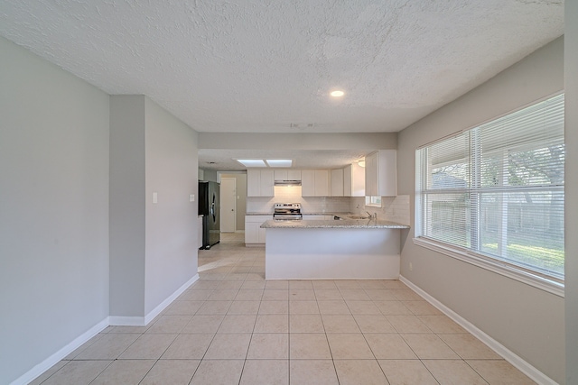 kitchen featuring backsplash, baseboards, light tile patterned floors, stainless steel electric range, and freestanding refrigerator