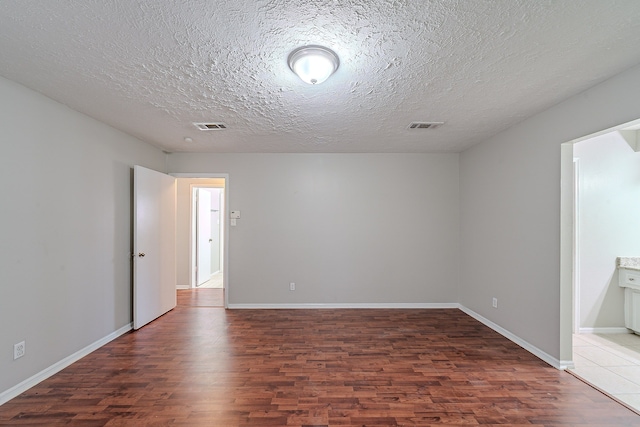 unfurnished room featuring visible vents, a textured ceiling, baseboards, and wood finished floors