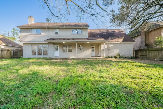 back of house with a lawn, brick siding, a fenced backyard, and a chimney