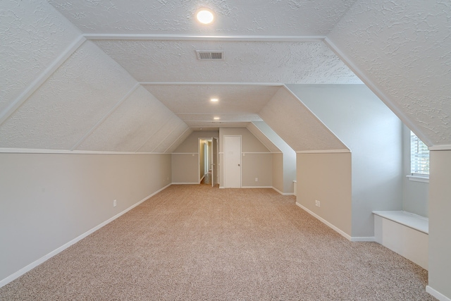 additional living space with vaulted ceiling, visible vents, carpet floors, and a textured ceiling