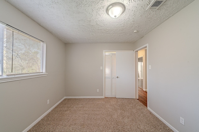 carpeted spare room with visible vents, a textured ceiling, and baseboards