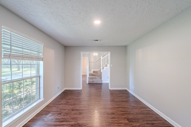 unfurnished room featuring visible vents, baseboards, stairway, a textured ceiling, and dark wood-style flooring