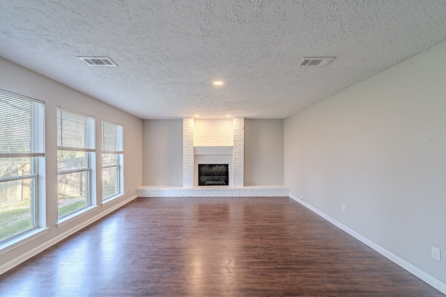 unfurnished living room featuring visible vents, a brick fireplace, baseboards, dark wood-style floors, and a textured ceiling