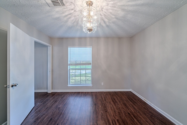 spare room with visible vents, dark wood-type flooring, a textured ceiling, baseboards, and a chandelier