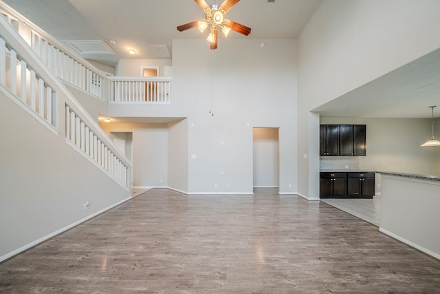 unfurnished living room featuring baseboards, a ceiling fan, light wood-style floors, and a towering ceiling