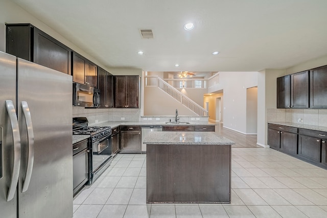 kitchen featuring light tile patterned flooring, a kitchen island, black appliances, and a sink