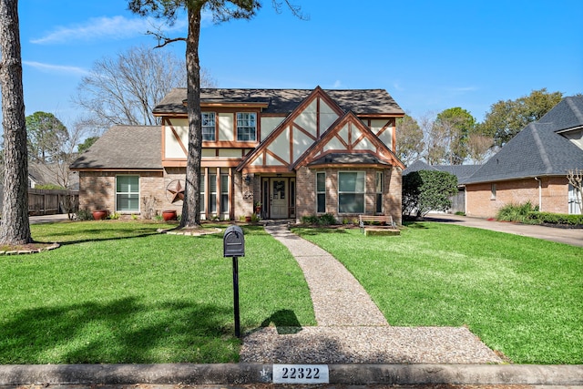 english style home with brick siding, a shingled roof, and a front lawn