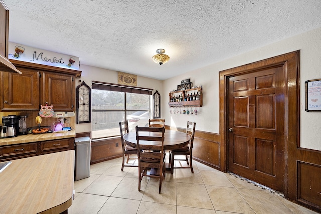 dining room featuring a textured ceiling, light tile patterned floors, and wainscoting