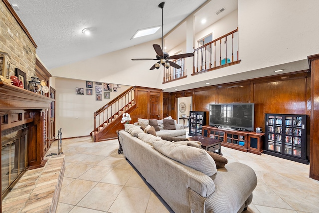 living room featuring light tile patterned floors, ceiling fan, stairs, a textured ceiling, and a large fireplace