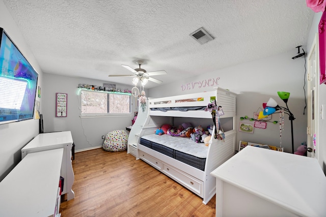 bedroom featuring visible vents, a ceiling fan, a textured ceiling, light wood-style floors, and baseboards