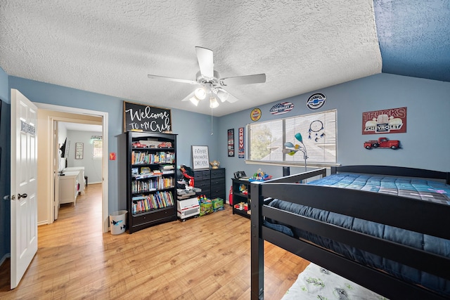 bedroom featuring ceiling fan, vaulted ceiling, light wood-type flooring, and a textured ceiling