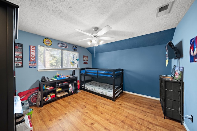 bedroom with wood finished floors, visible vents, baseboards, vaulted ceiling, and a textured ceiling