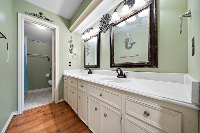 bathroom featuring double vanity, toilet, wood finished floors, and a sink