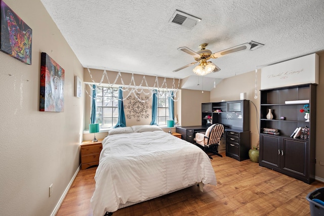 bedroom with visible vents, baseboards, light wood-style floors, a textured ceiling, and a ceiling fan