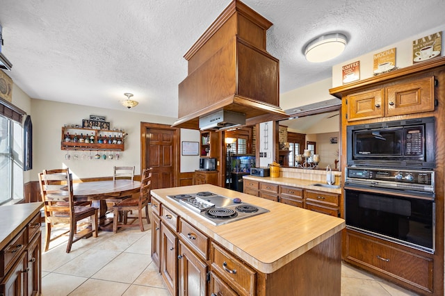 kitchen featuring black appliances, light tile patterned floors, brown cabinetry, and a kitchen island