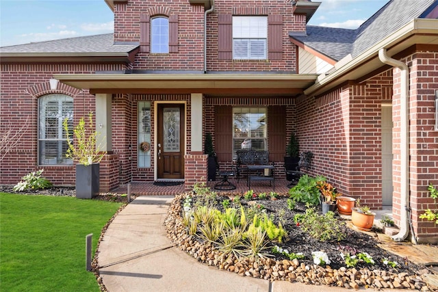 property entrance featuring a yard, brick siding, and roof with shingles