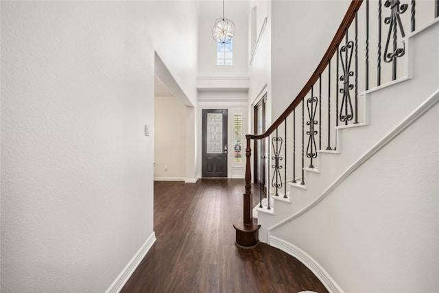 foyer entrance with baseboards, dark wood finished floors, a high ceiling, stairs, and a chandelier