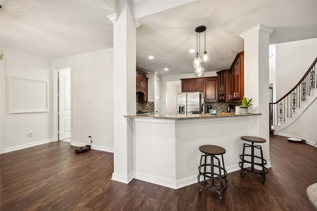 kitchen with dark wood-type flooring, light stone counters, stainless steel fridge, and decorative columns