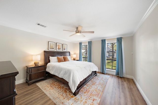 bedroom with a ceiling fan, visible vents, wood finished floors, baseboards, and ornamental molding