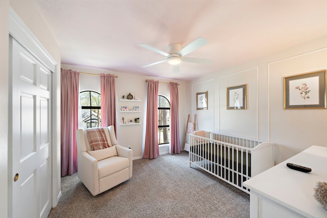 bedroom with light carpet, a crib, and a ceiling fan