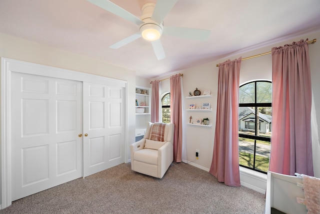 living area featuring baseboards, light colored carpet, and a ceiling fan