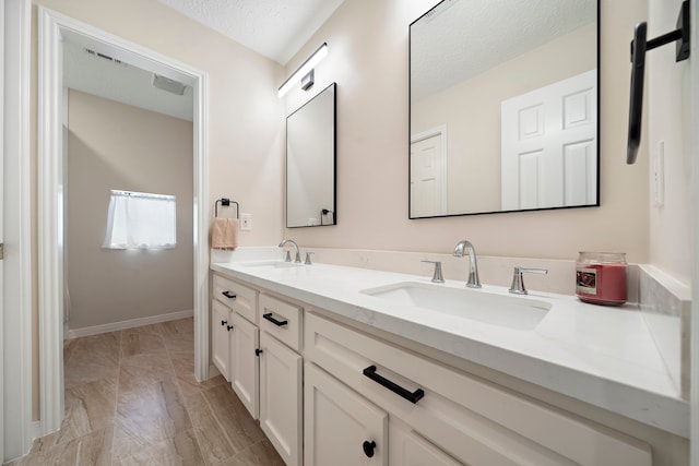 bathroom with a textured ceiling, double vanity, baseboards, and a sink