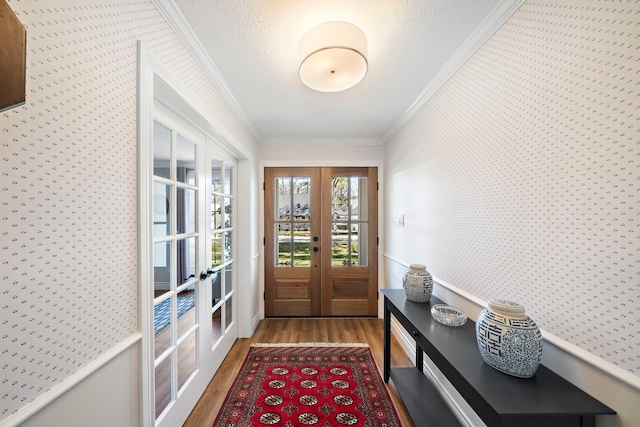 entrance foyer with french doors, wood finished floors, crown molding, and wallpapered walls