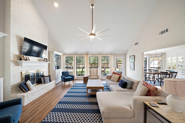 living room featuring visible vents, high vaulted ceiling, a brick fireplace, and wood finished floors