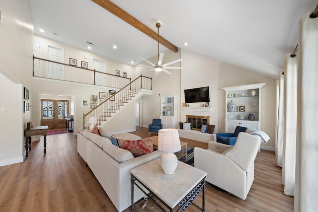 living area with wood finished floors, a fireplace, stairs, french doors, and beamed ceiling