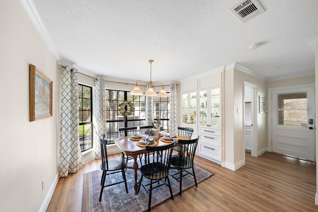 dining space with visible vents, ornamental molding, a textured ceiling, and wood finished floors