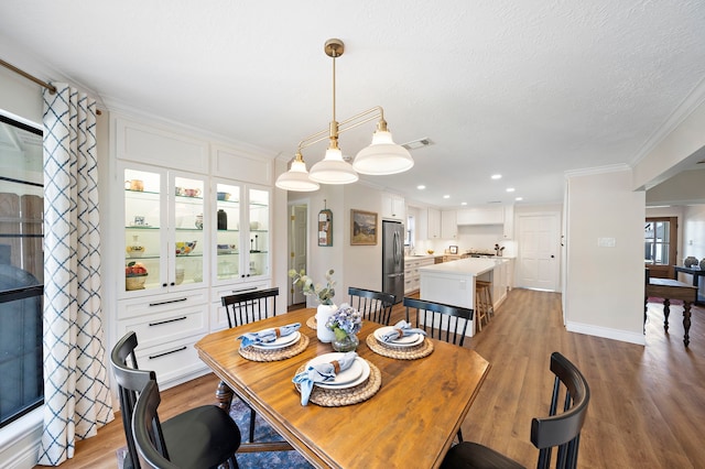 dining area with light wood-type flooring, visible vents, ornamental molding, a textured ceiling, and recessed lighting