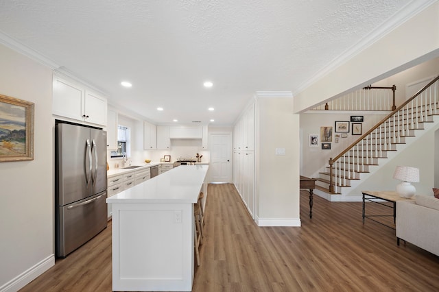 kitchen featuring light wood finished floors, ornamental molding, stainless steel appliances, white cabinets, and light countertops