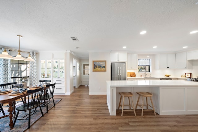 kitchen featuring visible vents, light countertops, wood finished floors, stainless steel refrigerator, and a sink