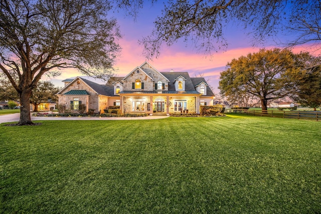 back of property at dusk featuring stone siding, a lawn, a standing seam roof, and fence