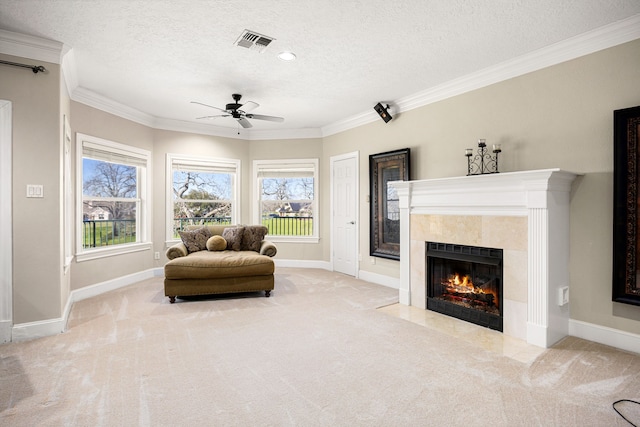 living area featuring visible vents, a textured ceiling, a tiled fireplace, crown molding, and carpet flooring