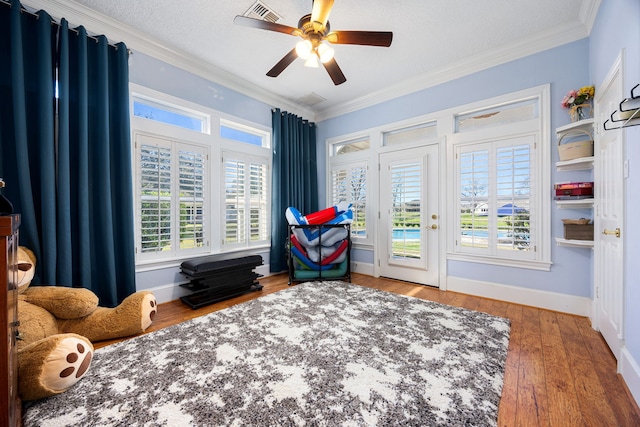 interior space featuring visible vents, ornamental molding, a ceiling fan, hardwood / wood-style floors, and baseboards