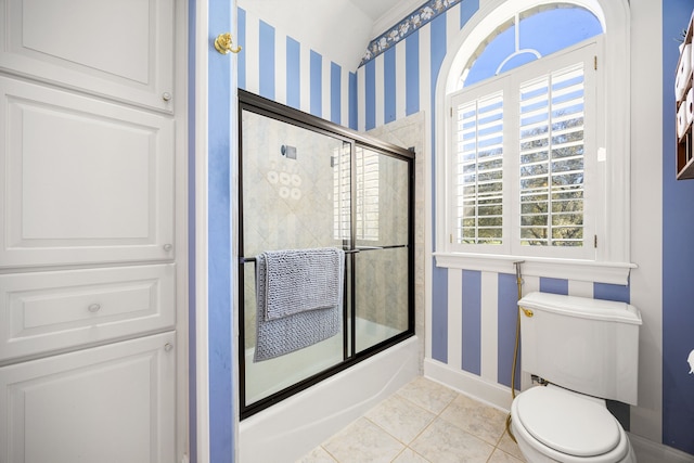 bathroom with wallpapered walls, baseboards, toilet, shower / bath combination with glass door, and tile patterned floors