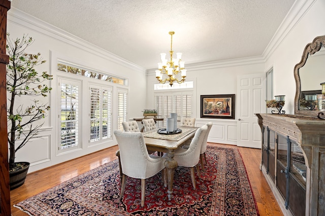 dining area with a notable chandelier, light wood-style flooring, a textured ceiling, and crown molding