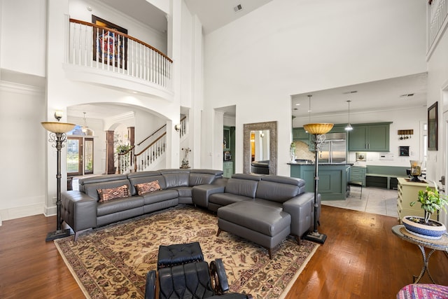 living area with stairs, crown molding, wood finished floors, and arched walkways