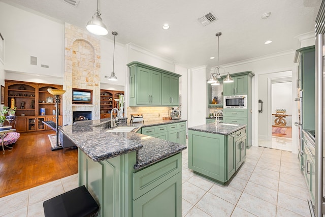 kitchen with green cabinets, stainless steel microwave, a kitchen island with sink, and visible vents