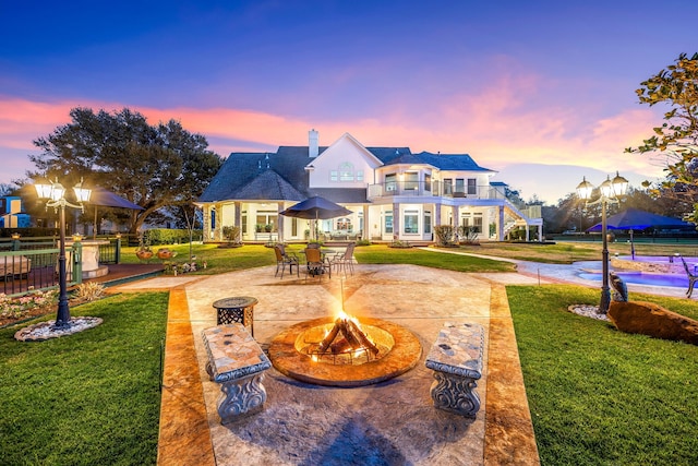 rear view of house with a patio, a balcony, fence, an outdoor fire pit, and a lawn