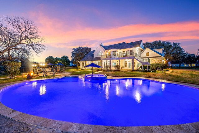 pool at dusk with a pool with connected hot tub, fence, stairway, a yard, and a patio area