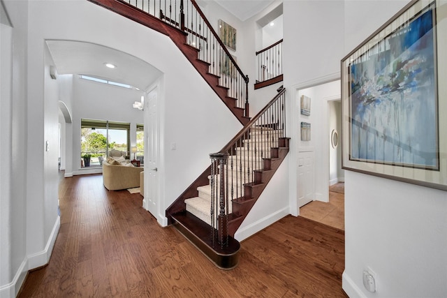 entrance foyer featuring baseboards, stairway, a towering ceiling, wood finished floors, and arched walkways