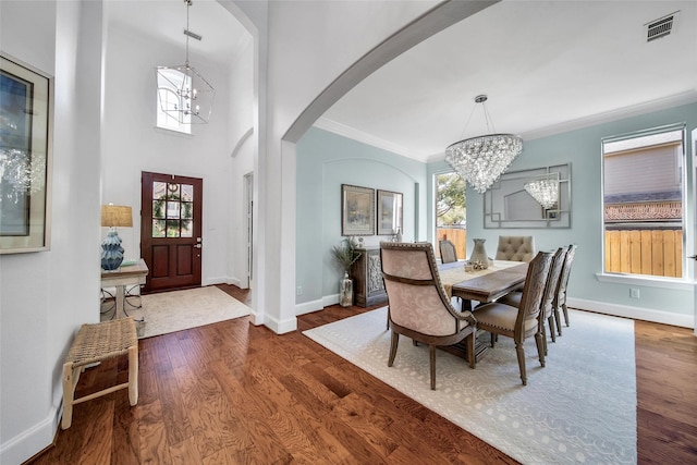 dining area with wood finished floors, baseboards, an inviting chandelier, arched walkways, and crown molding