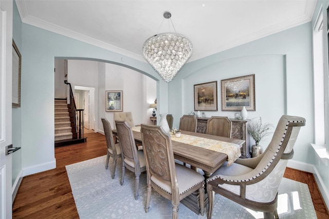 dining space with stairway, ornamental molding, an inviting chandelier, wood finished floors, and arched walkways